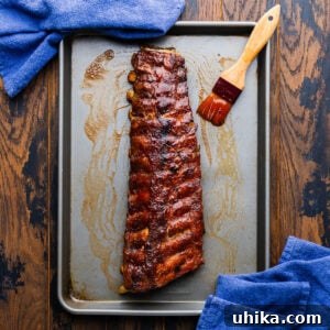 Rack of oven bbq ribs in sheet pan with brush covered with bbq sauce.