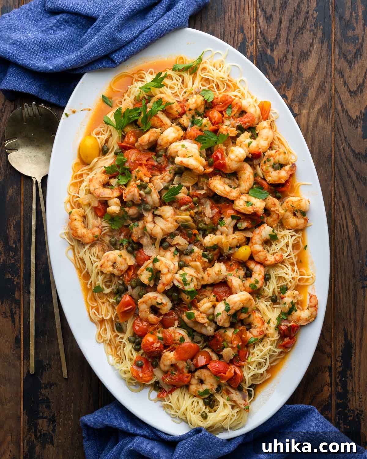 Effortless Old Bay Shrimp Capellini for Summer 2 Old Bay shrimp with capellini in white platter with blue napkins and serving spoons, garnished with fresh parsley and lemon wedges.