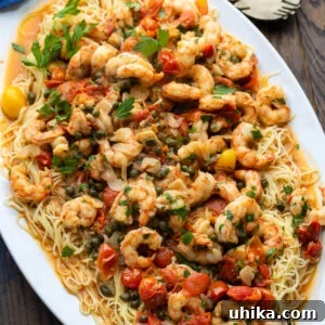 Old Bay shrimp with capellini in white platter, garnished with fresh herbs and serving utensils.