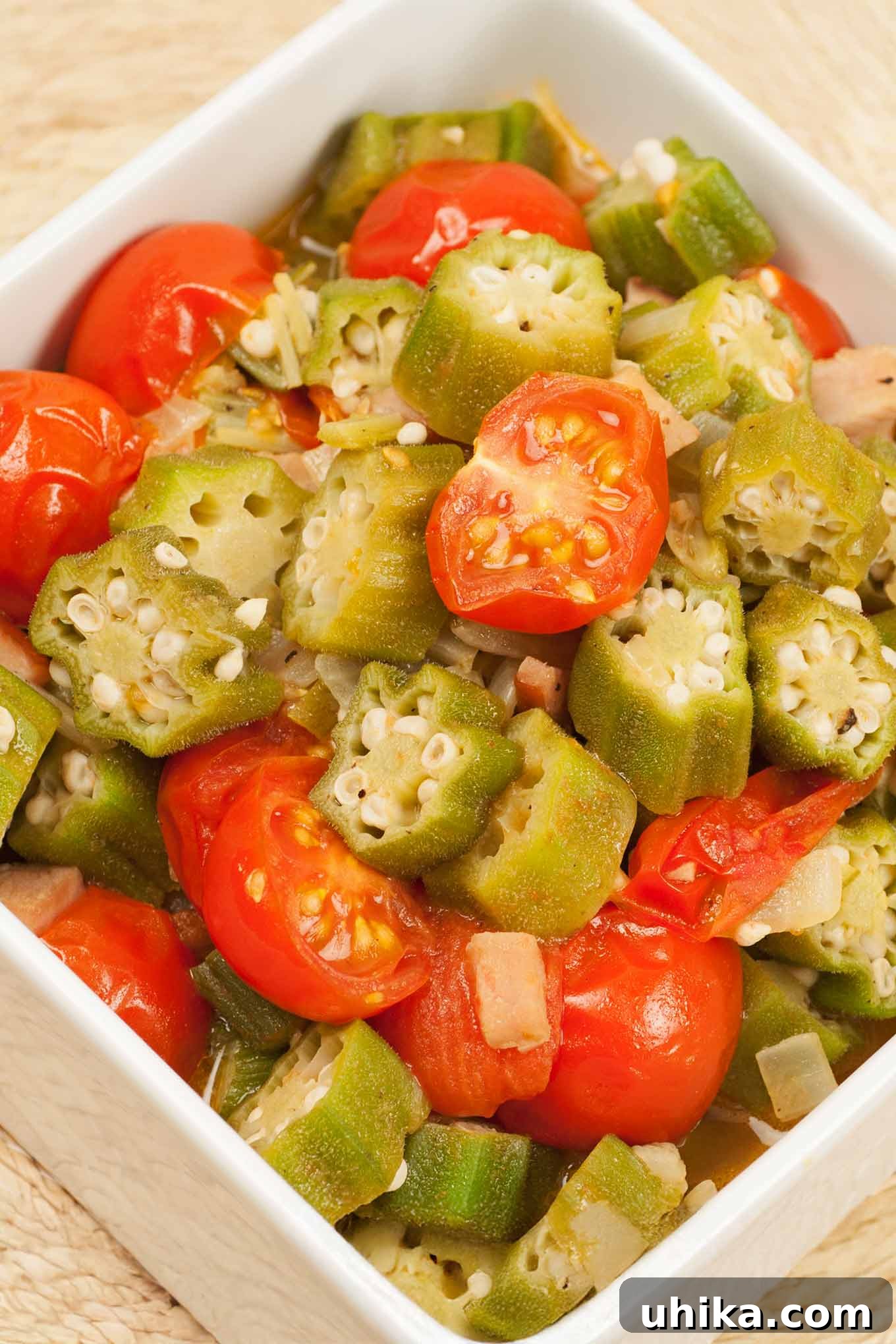 A vibrant, healthy side dish of sautéed okra and halved cherry tomatoes, seasoned with sweet onion and garlic, served in a white bowl. Perfect for Southern meals.