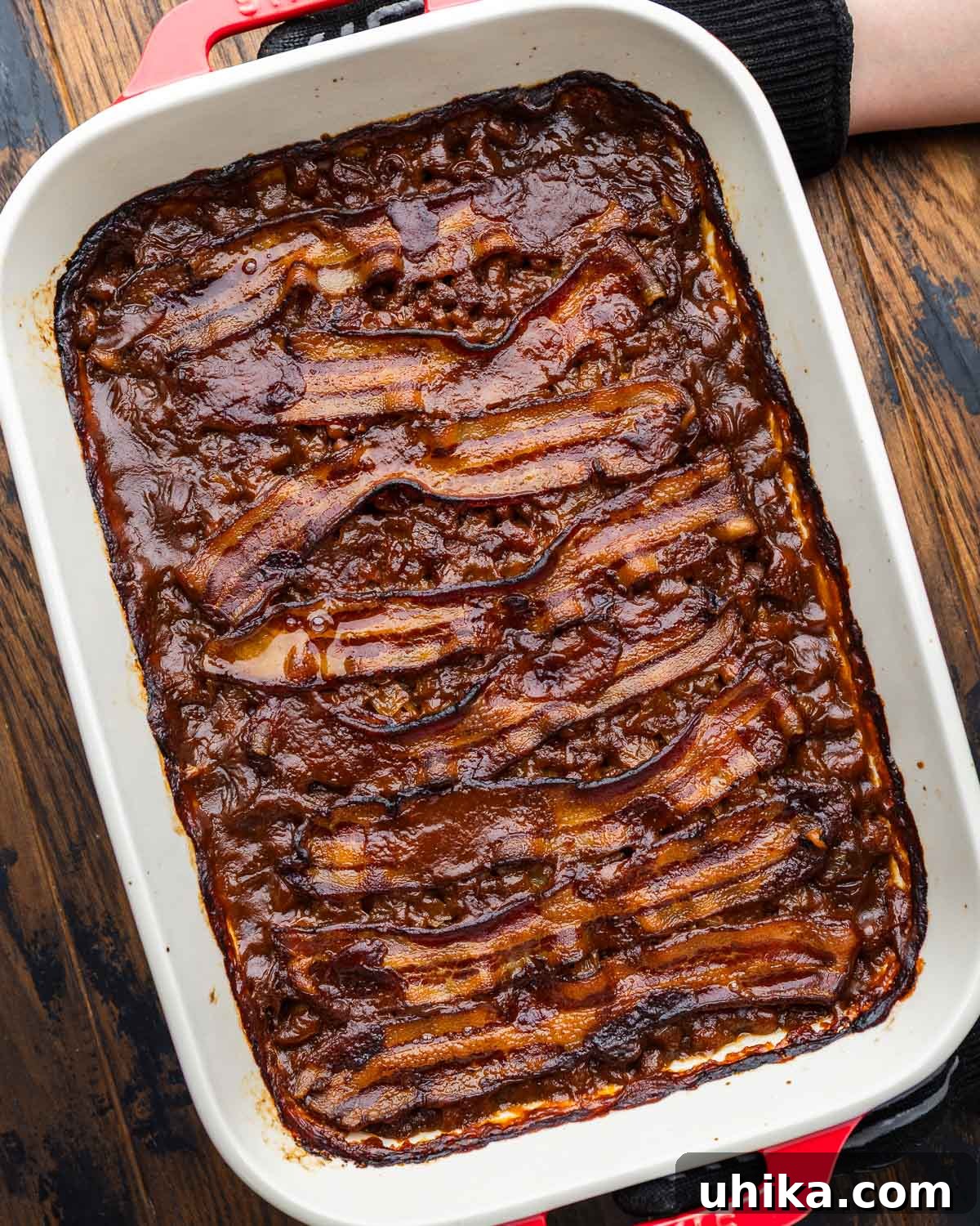Our Signature Summer Baked Beans 2 Hands holding a bowl of freshly baked beans topped with crispy bacon.
