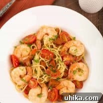 An overhead view of a serving of thin spaghetti tossed with chunks of chorizo, sautéed garlic and onion, jumbo shrimp simmered in sherry, and grape tomatoes.