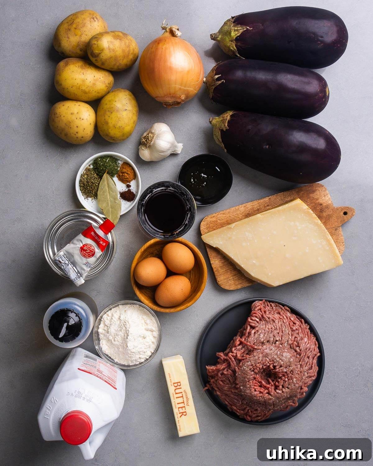 Greek Moussaka The Classic Eggplant and Beef Bake 4 A vibrant display of fresh Moussaka recipe ingredients, including potatoes, onion, eggplants, garlic, a selection of spices, red wine, tomato paste, eggs, parmesan cheese, olive oil, flour, milk, butter, and lean ground beef.