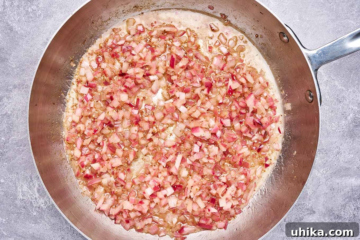 Hot Bacon Potato Salad 4 Preparation step for warm bacon dressing featuring an overhead view of a stainless frying pan with diced red onion sautéed in oil and bacon drippings.