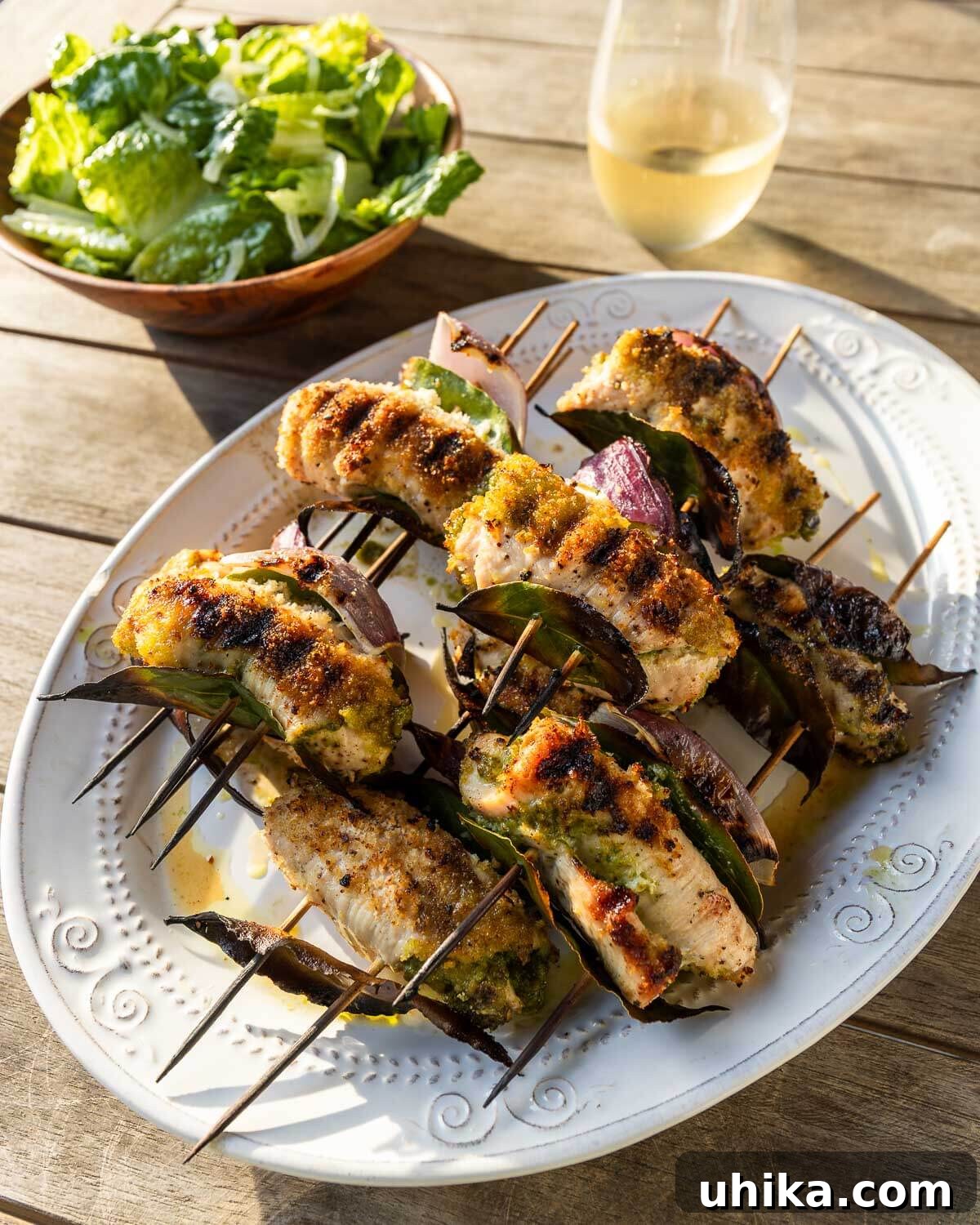 Sicilian Grilled Chicken Spiedini 2 Grilled Chicken Spiedini artfully arranged on a white platter, accompanied by a fresh green salad and a glass of white wine in a vibrant summer setting.