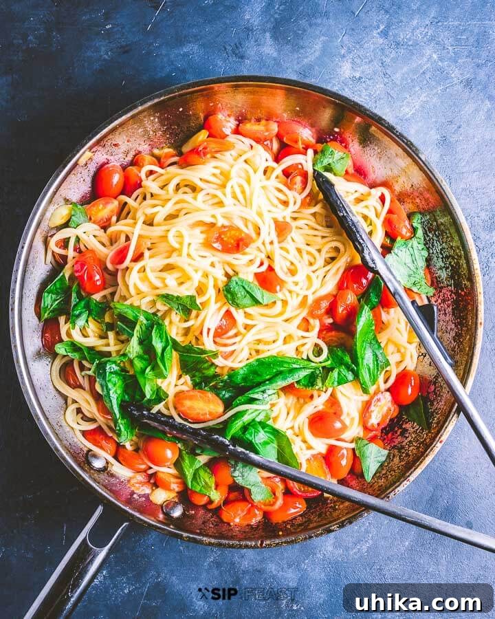 A finished pan of pasta with cherry tomatoes, basil, and garlic, garnished with fresh basil, ready to be served.