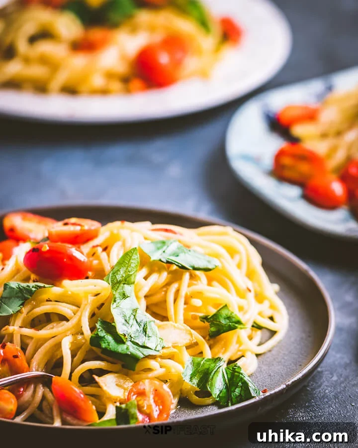 Three plates of spaghetti and cherry tomatoes on a blue setting, garnished with fresh basil leaves, ready to be served.