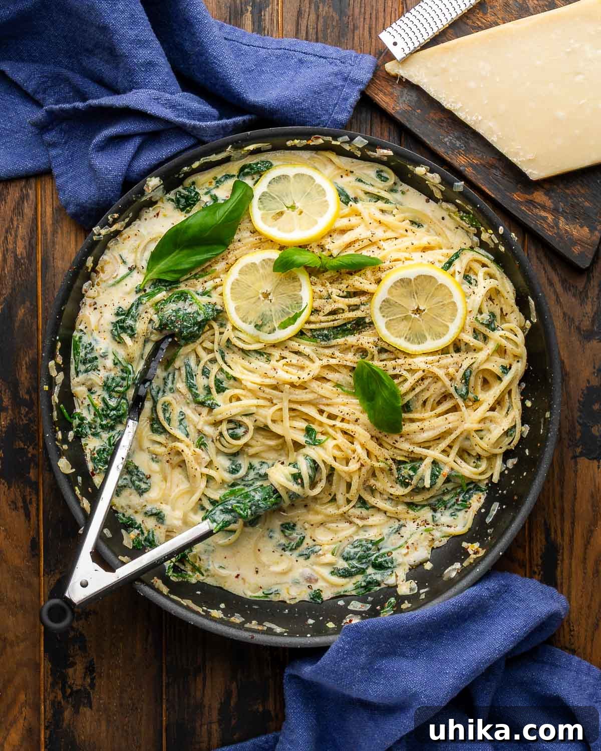 Zesty Lemon Ricotta Spinach Pasta 2 Large black pan filled with creamy lemon ricotta spinach pasta, garnished with fresh basil and a block of parmesan cheese nearby.