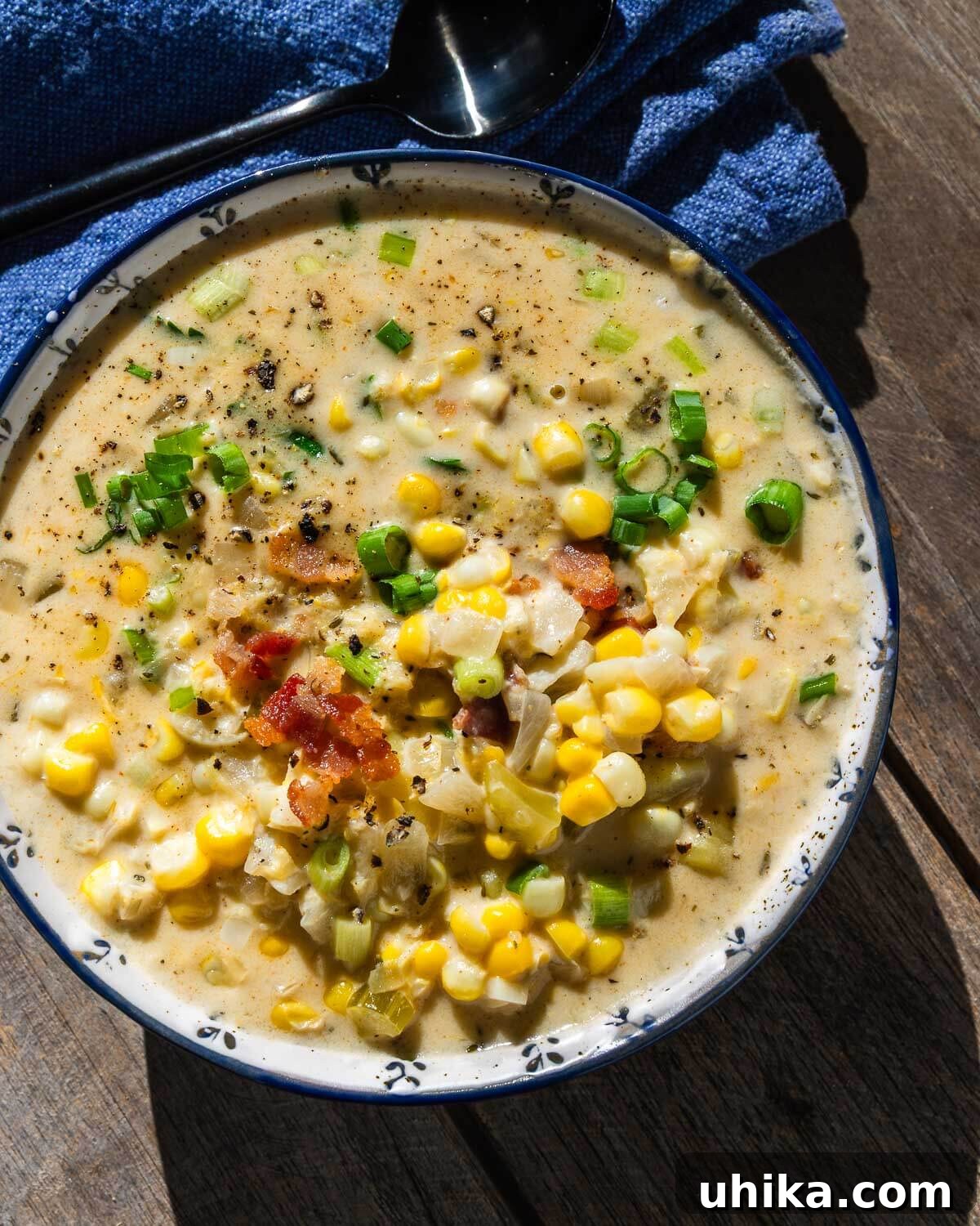 Creamy Golden Corn Chowder 2 A steaming bowl of creamy corn chowder, garnished with green onions and bacon, illuminated by natural sunlight.