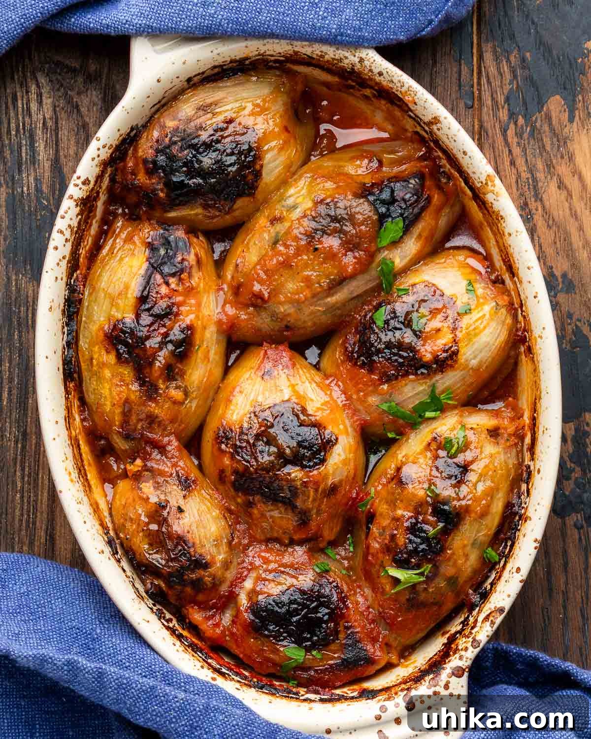 Savory Greek Onion Bake 2 Greek stuffed onions baked to perfection in a ceramic baking dish, showcasing their tender, golden-brown exterior and rich tomato sauce.