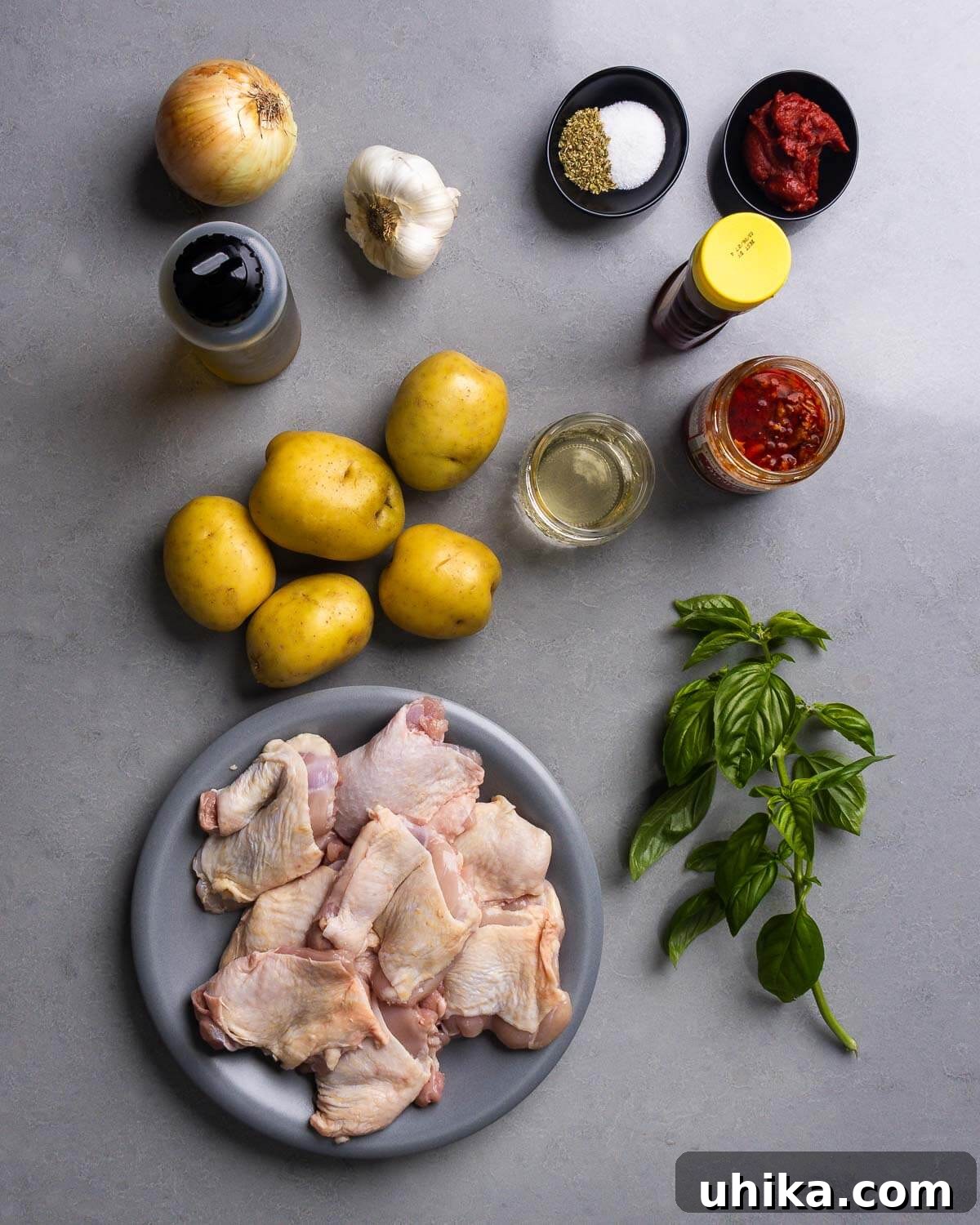 Sticky Hot Honey Chicken and Potatoes 4 Ingredients shown for One-Pan Hot Honey Chicken and Potatoes: onion, olive oil, garlic, oregano, salt, tomato paste, honey, potatoes, wine, Calabrian chili paste, chicken thighs, and basil.