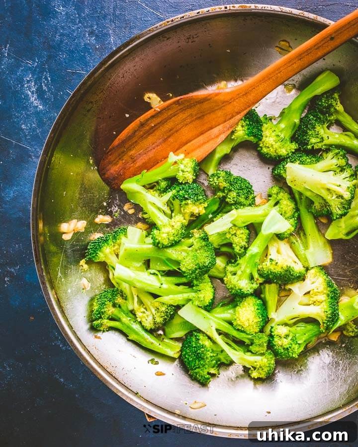 Freshly Cooked Italian Broccoli - Ready to serve side dish. #broccoli #garlic #oliveoil Perfectly sautéed garlic broccoli in a pan, glistening with olive oil, on a rustic blue background.