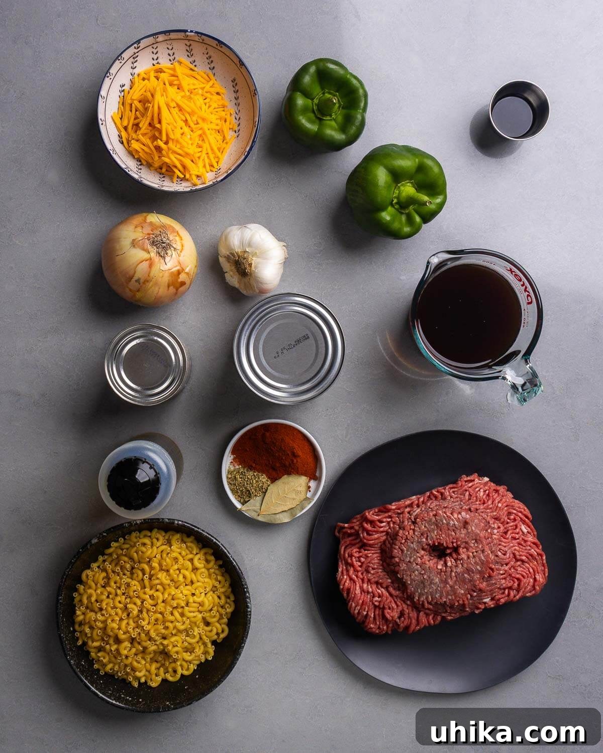 Homestyle American Beef and Macaroni 4 Various ingredients for American goulash laid out on a table, including shredded cheddar cheese, bell peppers, soy sauce, Worcestershire sauce, onion, garlic, canned tomatoes, beef stock, olive oil, spices, elbow macaroni, and ground beef.