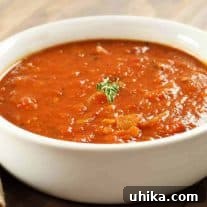 Bacon and tomato soup served in a white bowl, garnished with a small sprig of fresh thyme.