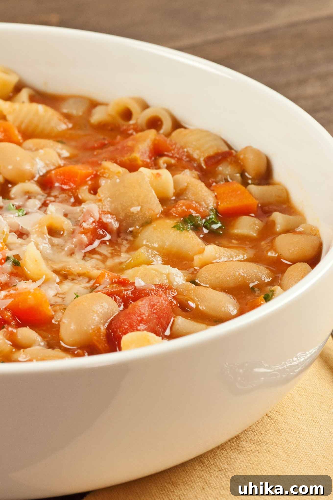 Hearty Italian Pasta and Bean Soup 2 A close-up of a white bowl filled with pasta e fagioli soup, showing pasta, beans, and vegetables in a broth, garnished with fresh parsley and grated cheese.