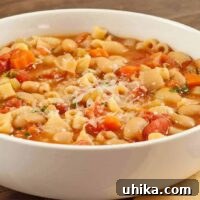 A close-up of a white bowl filled with pasta e fagioli soup, showing pasta, beans, and vegetables in a broth.