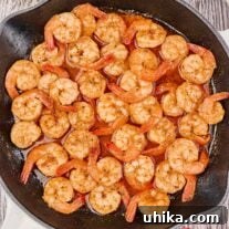 A cast iron skillet filled with sautéed shrimp in a sauce of butter, Old Bay seasoning, Worcestershire, Tabasco, and thyme.