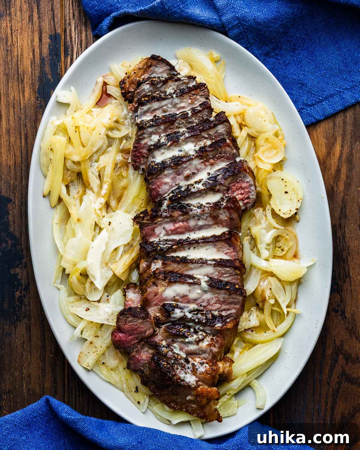 Perfectly seared New York strip steak with a luscious gorgonzola sauce, elegantly served on a bed of wilted fennel and onion, ready to be enjoyed.