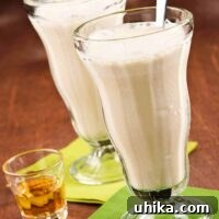 Two tall milkshake glasses filled with Bailey’s Irish Cream milkshake, served with an extra shot of Irish cream on the side.