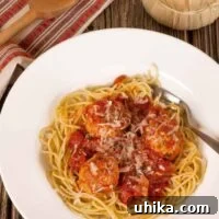 A plate of spaghetti topped with meatballs in marinara sauce, garnished with grated Parmesan cheese, on a wooden table with a napkin, wooden spoon, and a bottle of Chianti.