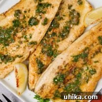 A serving plate of trout meunière topped with lemon, parsley, and minced shallot butter, garnished with lemon wedges and parsley.