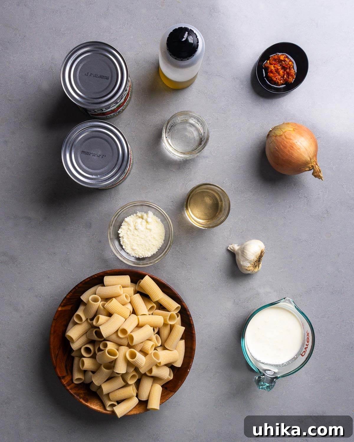 Crispy Chicken Cutlets with Fiery Vodka Rigatoni 4 Ingredients shown: 2 cans of plum tomatoes, olive oil, Calabrian chili paste, vodka, wine, onion, pecorino, garlic, rigatoni, and cream, laid out on a kitchen counter.