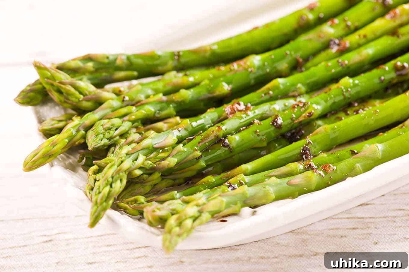 A vibrant display of steamed asparagus spears, glistening with a rich balsamic brown butter sauce on a pristine white serving plate, inviting diners to savor its gourmet appeal.