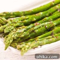 A close-up of beautifully plated steamed asparagus spears, elegantly coated in a glistening balsamic brown butter sauce.