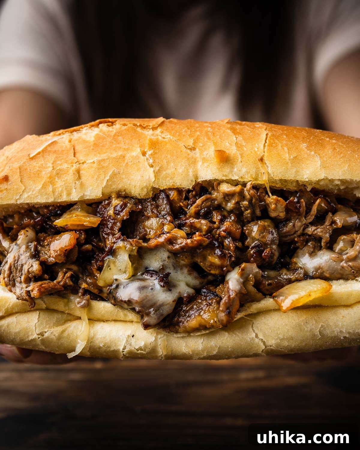 Effortless Philly Cheesesteak 2 Hands holding a freshly made, hot Philly Cheesesteak with melted cheese and steak. A classic American sandwich.