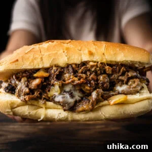 Hands holding Philly cheesesteak over table.