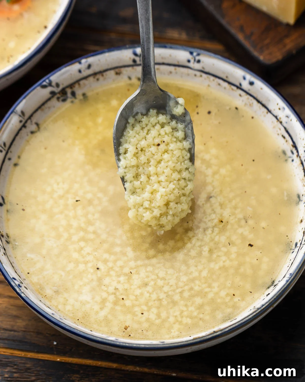 Heartwarming Pastina Broth 2 A spoonful of pastina being lifted from a bowl of golden Pastina in Brodo, showcasing the tiny pasta and rich, clear broth.