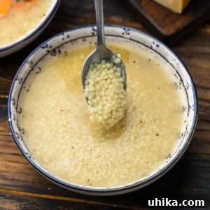 Heartwarming Pastina Broth 7 A spoonful of pastina held over a bowl of Pastina in Brodo, garnished with grated cheese.