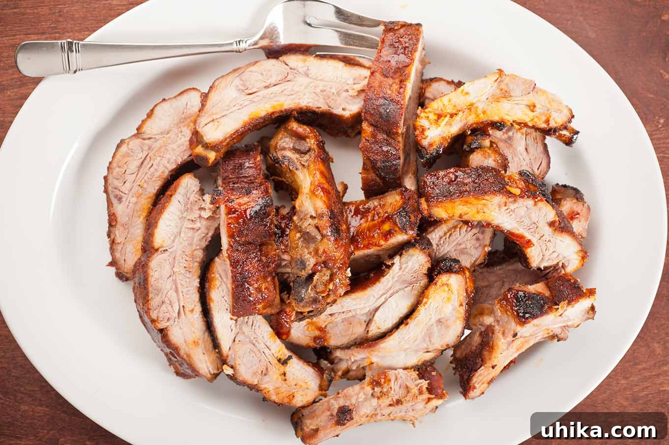 Fall-Off-The-Bone Oven Ribs 4 An oval serving plate piled with individual oven baked baby back ribs and a serving fork.