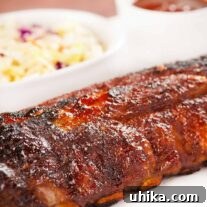 Fall-Off-The-Bone Oven Ribs 5 A close side view of a whole rack of baby back ribs, oven baked, glazed with homemade bourbon bbq sauce, coleslaw and more bbq sauce in the background.