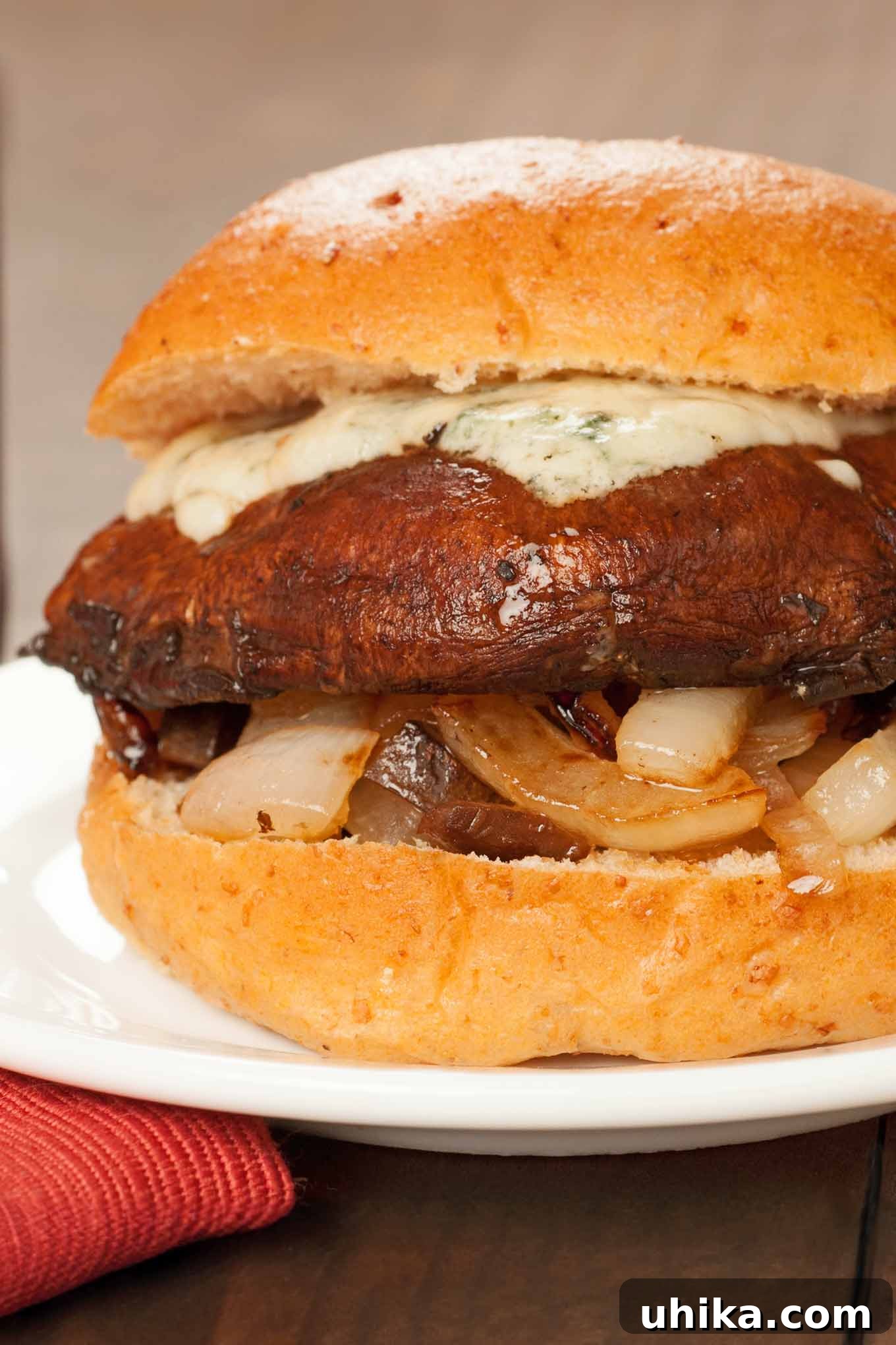 Gourmet Balsamic Portobello Burgers 2 A close-up view of a perfectly grilled portobello mushroom burger, generously topped with glistening caramelized onions and a rich, creamy layer of melted blue cheese. The dark, glossy balsamic glaze is visible on the mushroom cap, showcasing a truly appetizing vegetarian burger.