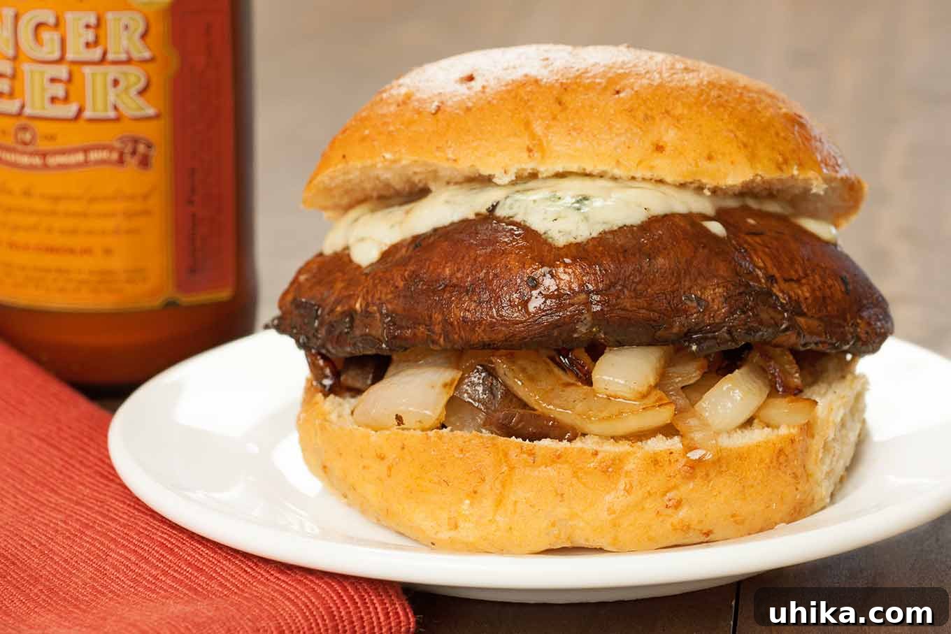 Gourmet Balsamic Portobello Burgers 3 A vibrant side view of a balsamic-glazed, grilled portobello mushroom served on a soft hamburger bun. It's generously layered with perfectly sautéed onions and topped with a creamy, melted gorgonzola blue cheese, making for an irresistibly delicious and healthy burger option.