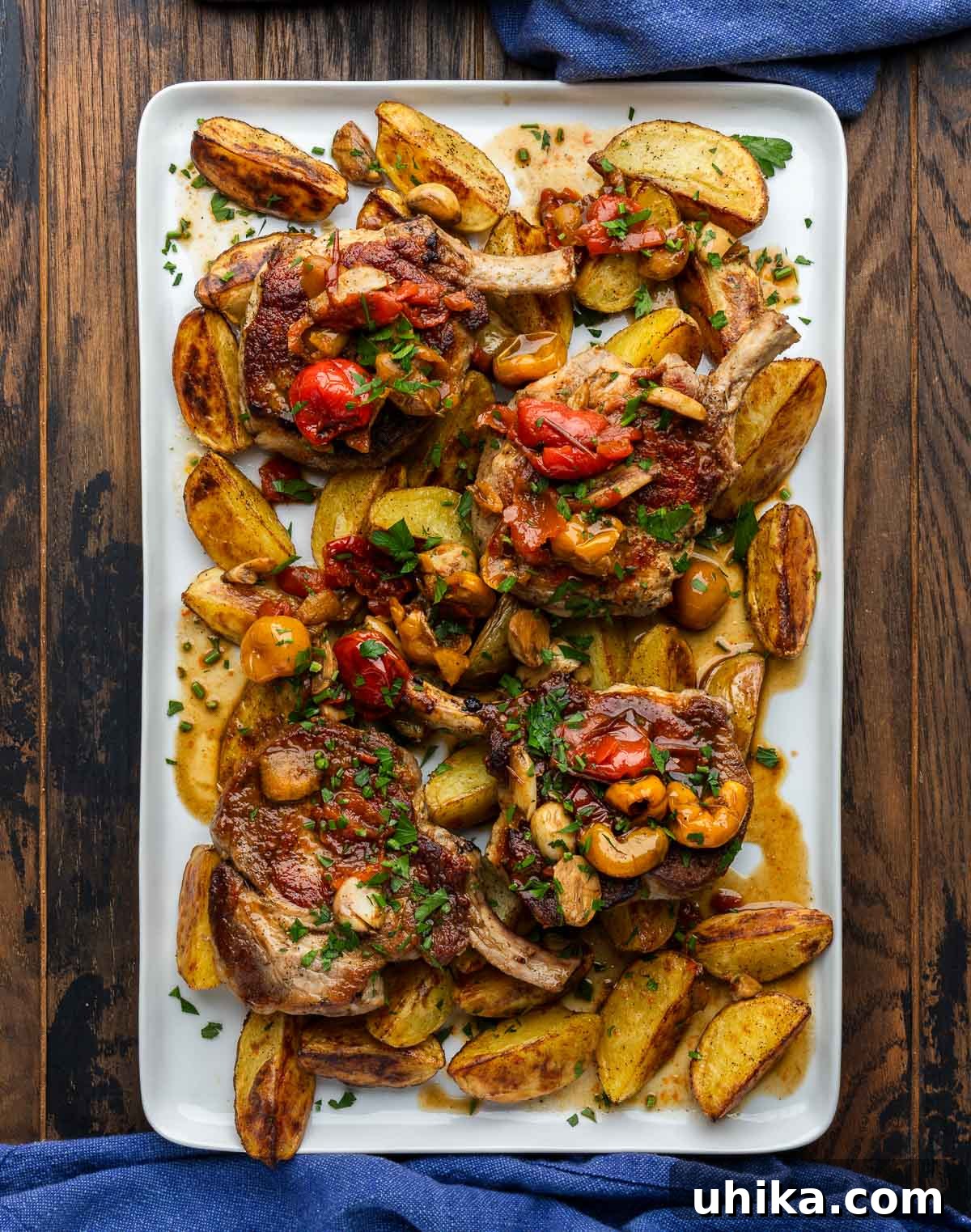 Sweet Heat Peppadew Pork with Crispy Roasted Potatoes 2 A large platter showcasing perfectly seared pork chops, golden roasted potatoes, and vibrant peppadew peppers, all drizzled with a rich, tangy sauce.