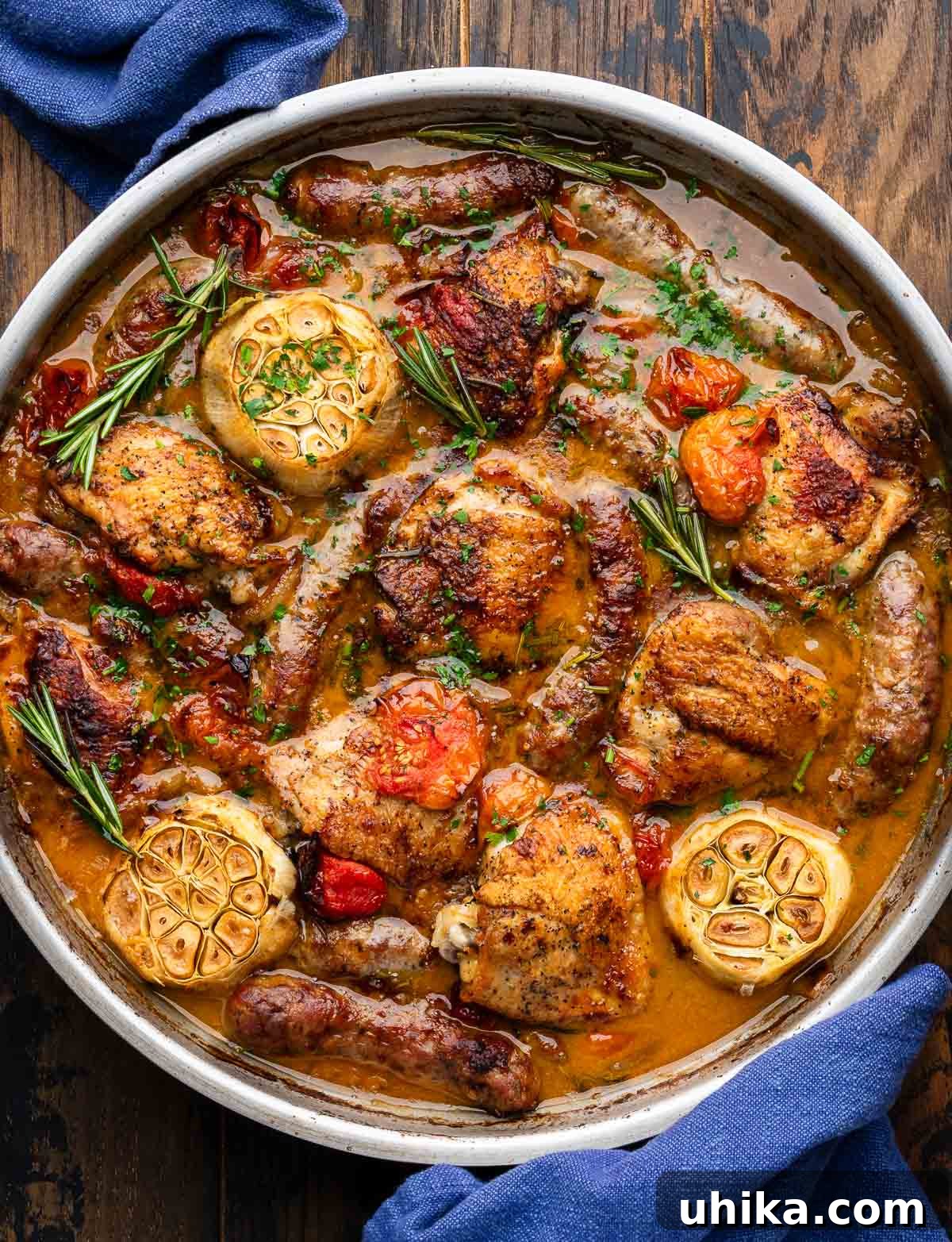 One-Pan Rosemary Chicken with Sausage and Burst Tomatoes 2 Rosemary chicken with sausage and tomatoes in a large pan, garnished with fresh herbs.
