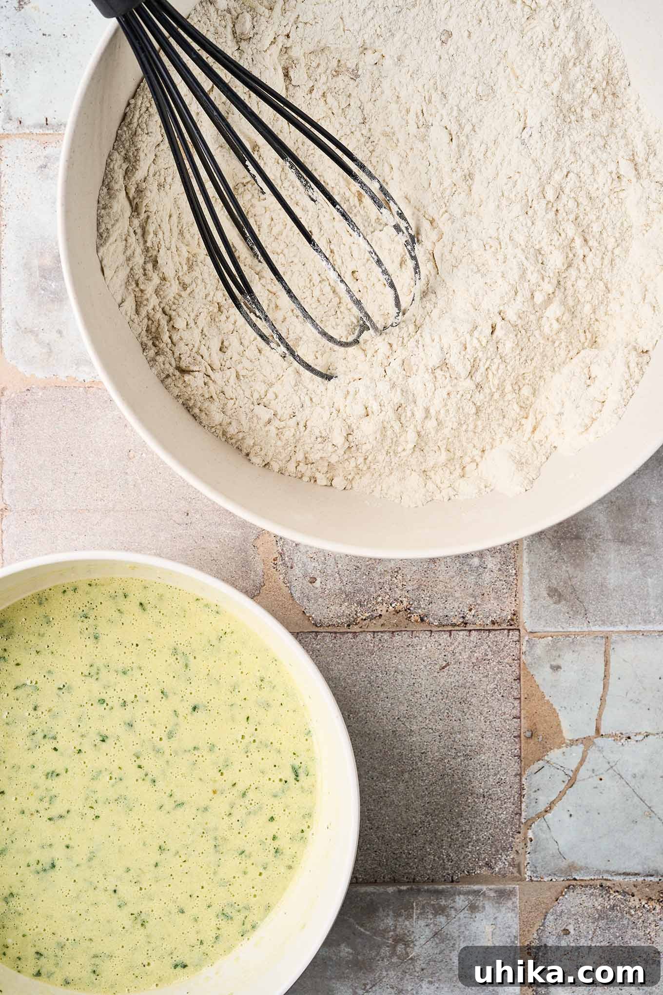 Hearty Savory Zucchini Bread 5 The dry ingredients for savory zucchini bread in a mixing bowl with a whisk beside a smaller mixing bowl containing the wet ingredients, ready to be combined.