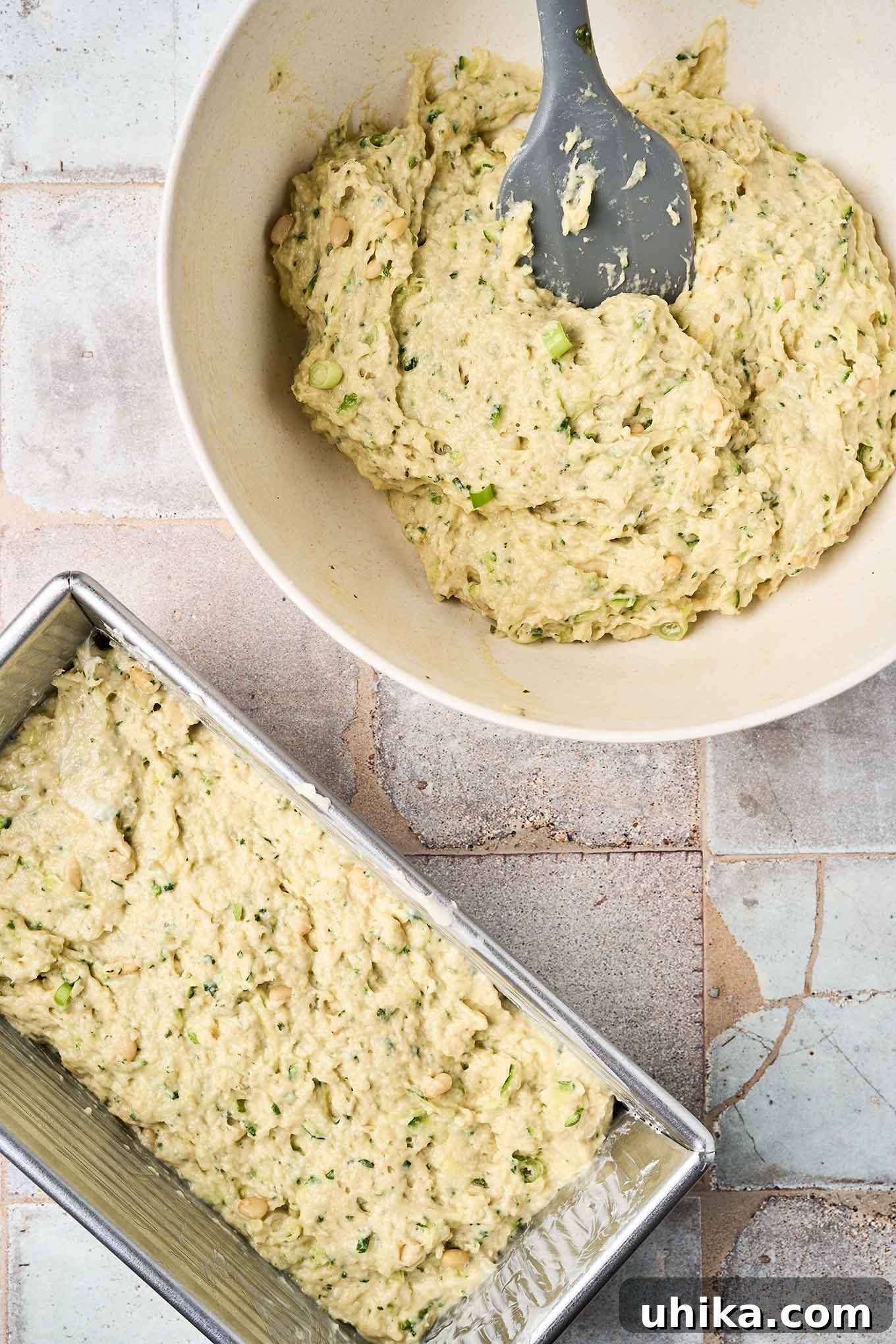 Hearty Savory Zucchini Bread 6 Pesto zucchini bread batter in a bowl with a spatula beside a loaf pan already filled and ready for baking.