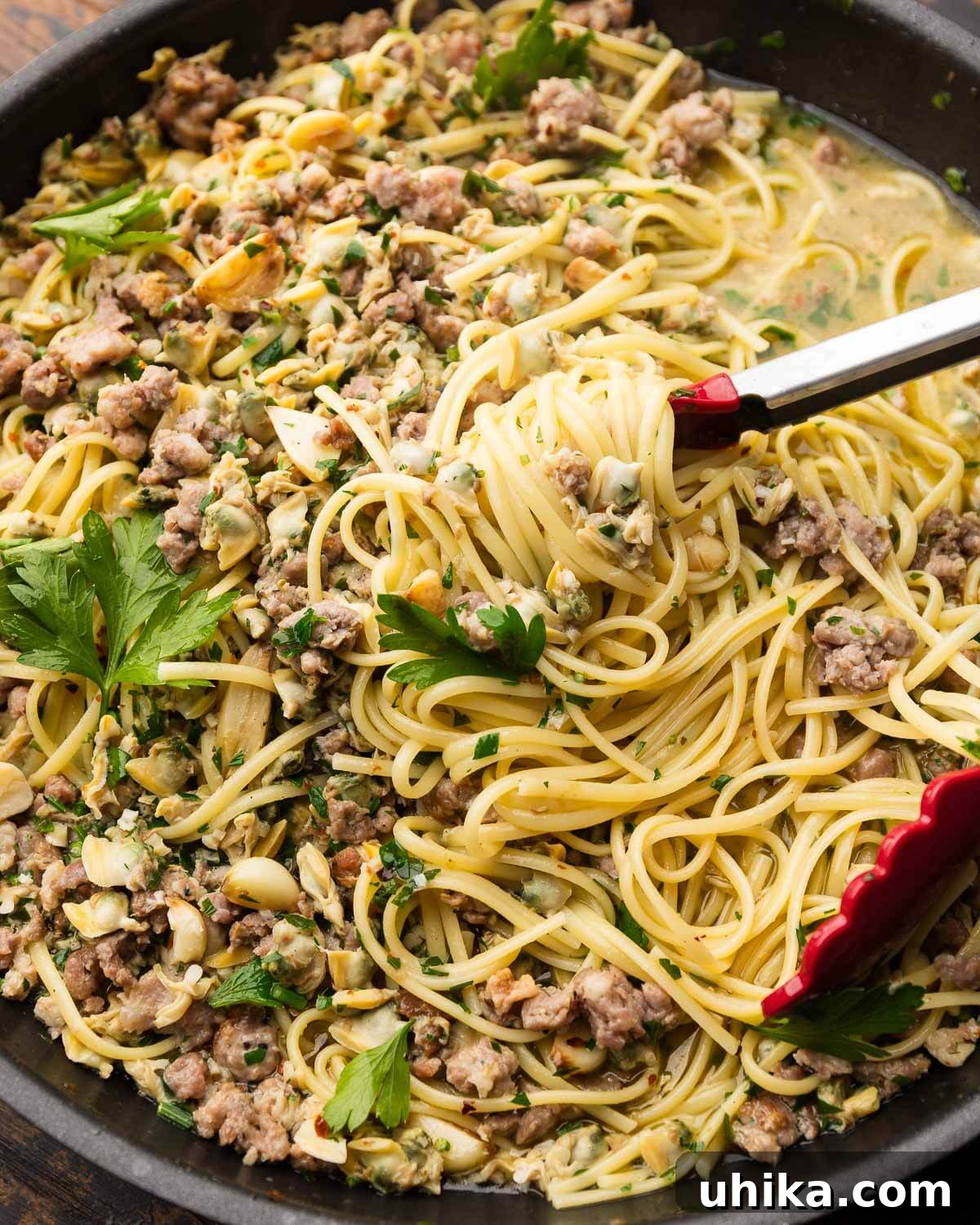 Rustic Sausage and Clam Linguine 2 Linguine with sausage and clams in black pan with red tongs.
