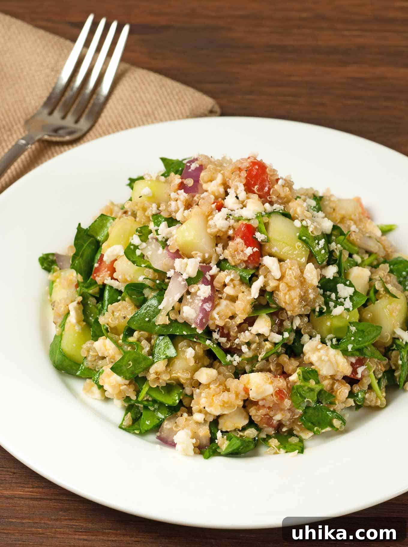 Zesty Greek Spinach Quinoa Salad 2 Greek spinach and quinoa salad with chopped cucumber, tomato, red onion, feta, and fresh greens on a white plate.