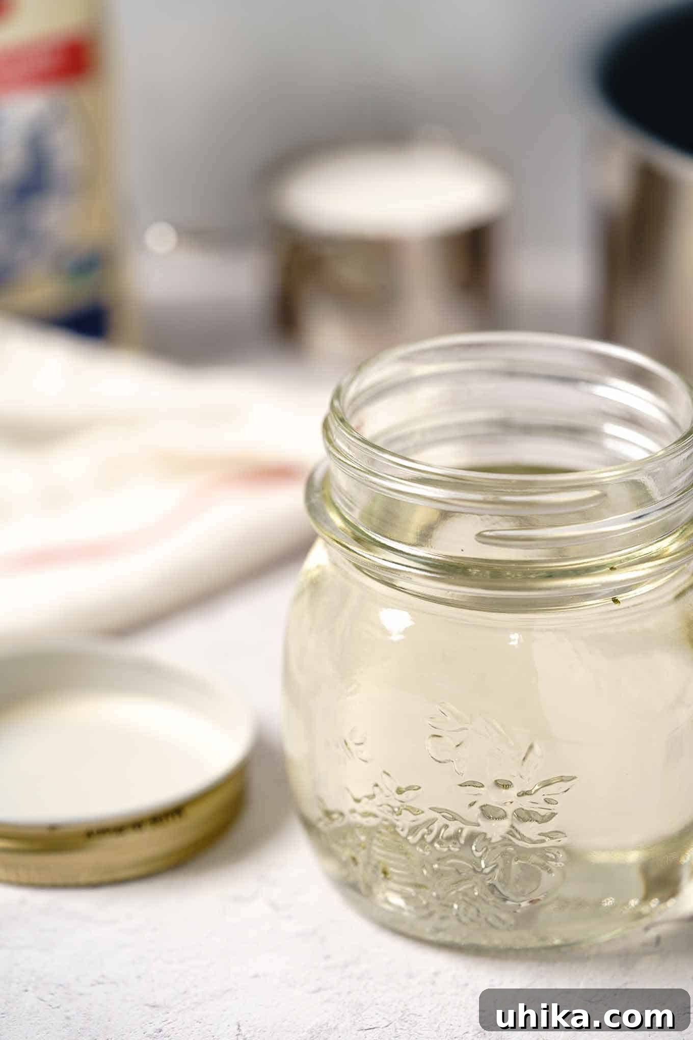 Easy Homemade Simple Syrup 2 A jar of freshly prepared simple syrup with a lid, alongside a bag of sugar, a measuring cup, and a saucepan in the background, ready for use in various beverages.