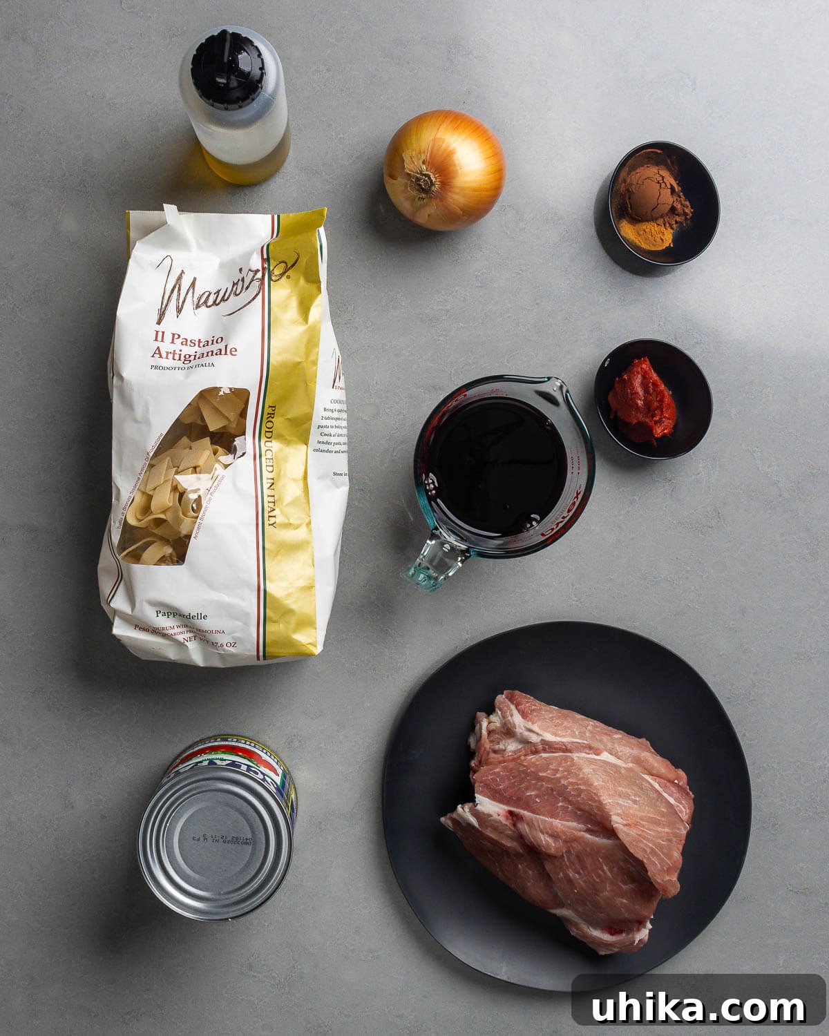 Slow Simmered Sicilian Pork Ragu 4 A vibrant display of fresh ingredients for Sicilian pork ragu, including olive oil, onion, cocoa powder, cinnamon, red wine, tomato paste, canned tomatoes, and cuts of pork shoulder.
