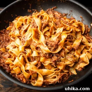 Black pan with pappardelle and Sicilian pork ragu, topped with grated cheese.