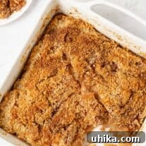 Apple brown betty with toasted cinnamon and crumb topping in a square white baking dish with one serving removed.