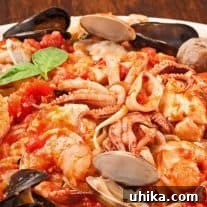A plate of linguine pasta topped with a medley of seafood including shrimp, mussels, clams, and squid in a rich tomato sauce, garnished with fresh basil leaves.