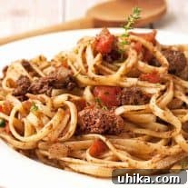 A plate of linguine topped with chicken liver ragu, featuring chunks of chicken liver, diced tomatoes, and fresh thyme.