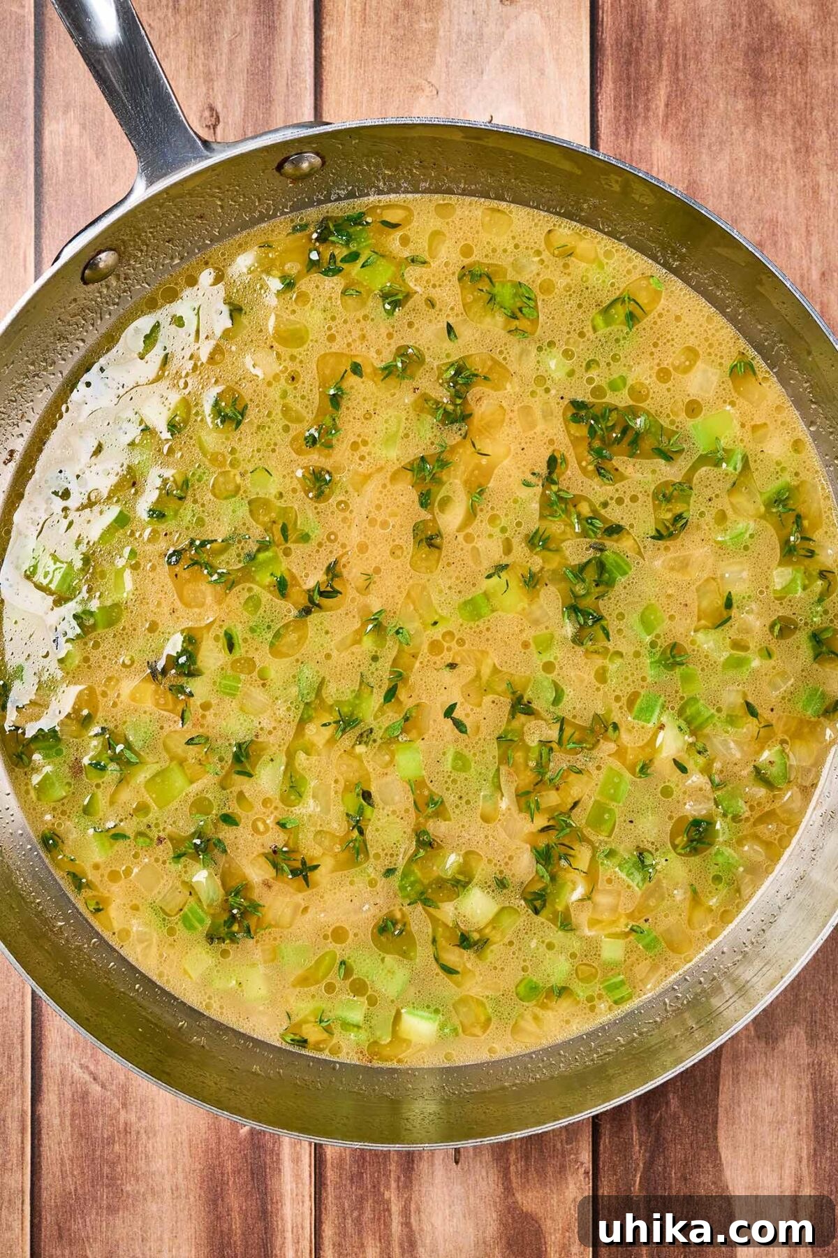 Smoked Bacon Cornbread Dressing 5 Cornbread stuffing preparation step two showing a pan with the sautéed aromatics, chicken broth, and butter needed to moisted the cornbread before baking.