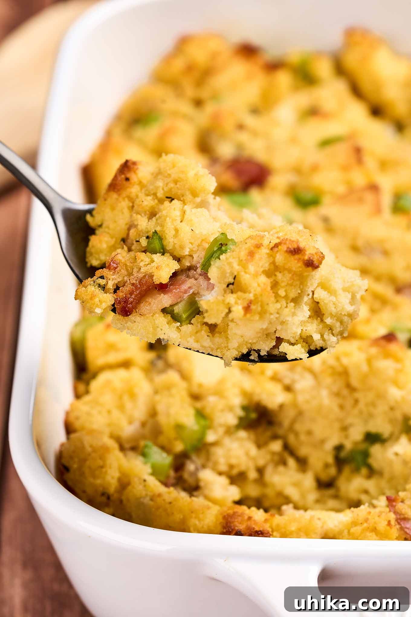 Smoked Bacon Cornbread Dressing 7 A serving of cornbread stuffing with bacon being spooned out of a white casserole dish.